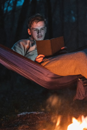 Reading a book while on a hammock sitting next to a campfire while backpacking overnight